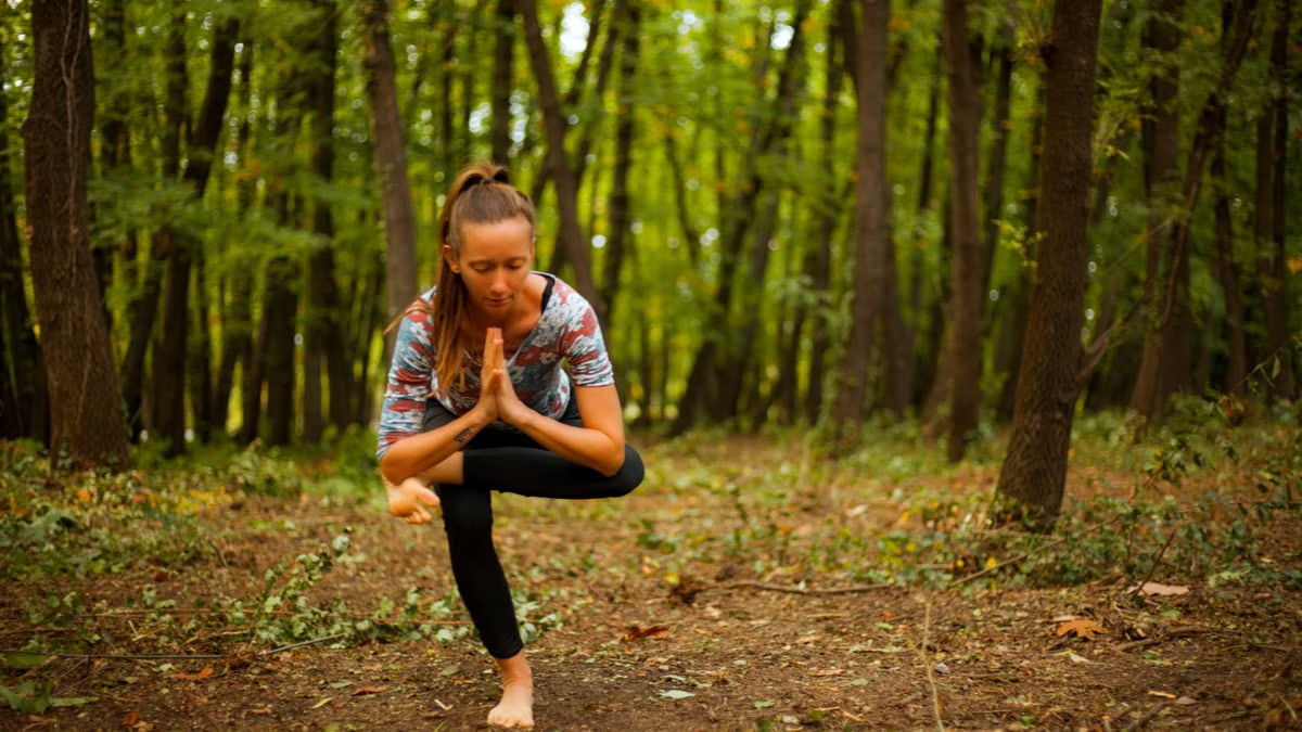 A woman meditates in a yoga pose amidst tranquil woods, focused on relaxation.
